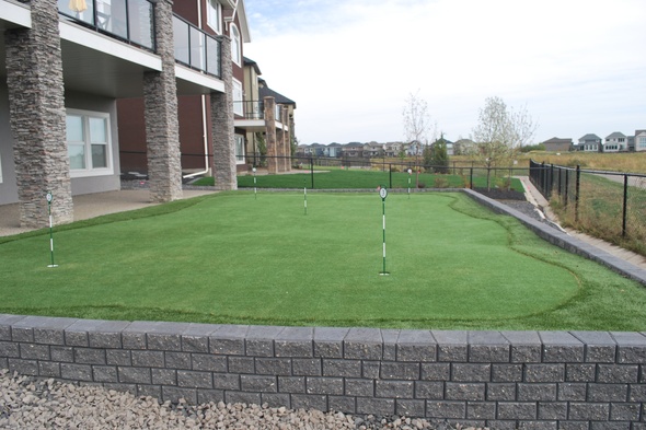 Kennewick residential backyard putting green grass near modern home with golf flags